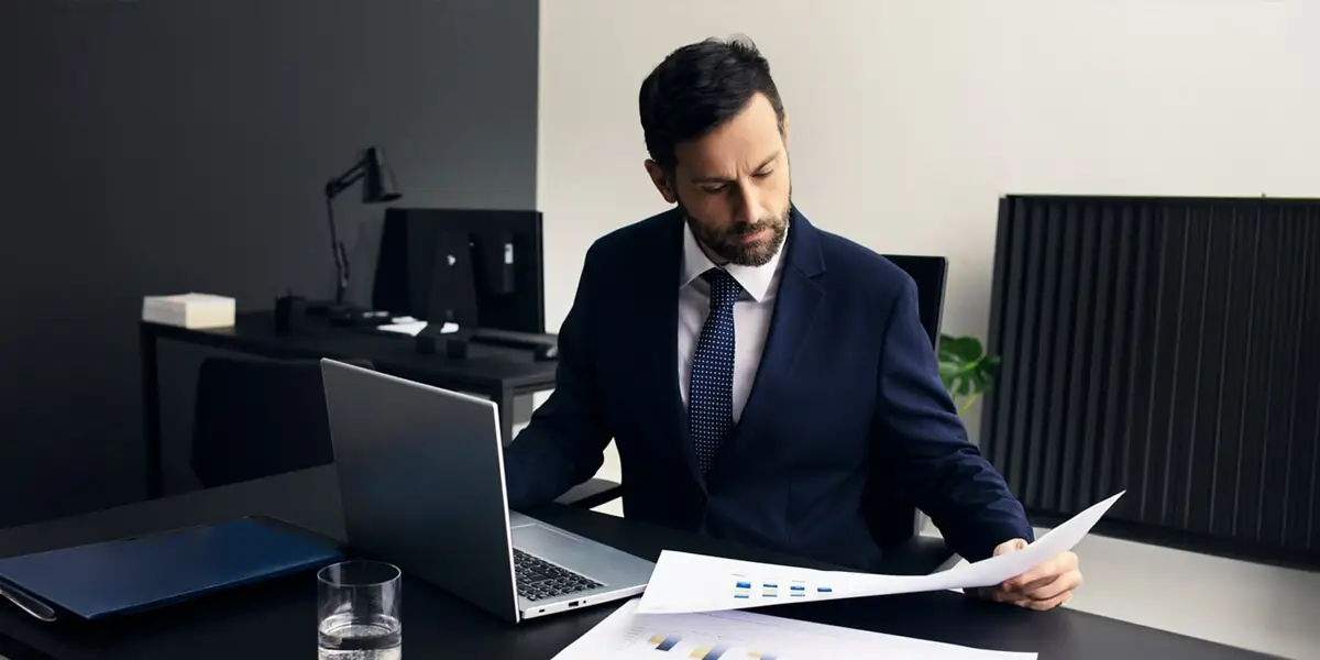 Uomo al computer che consulta documenti con dei grafici.